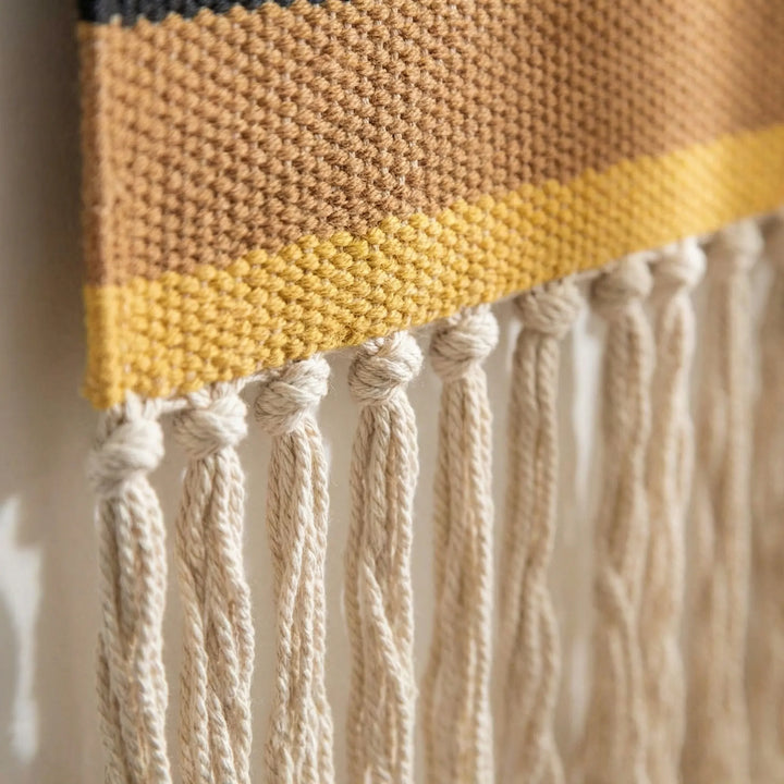 Woven art wall hanging with textured geometric patterns & fringe, perfect for bohemian home decor accents.