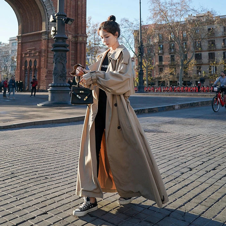 Full-length view of a women's double-breasted loose-fit trench coat, showcasing its long and fashionable style.