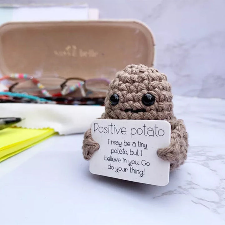 Positive potato knitted doll sitting on a desk with a tiny sign, offering encouragement & anxiety relief.