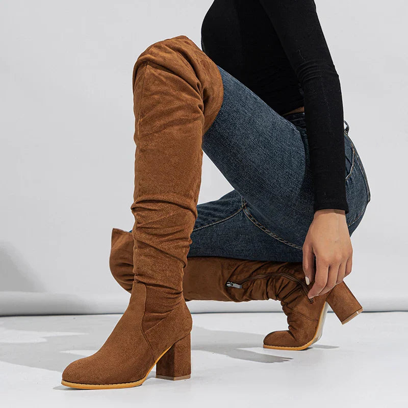 Woman wearing black over-the-knee heeled boots, styled with a dress for an elegant look