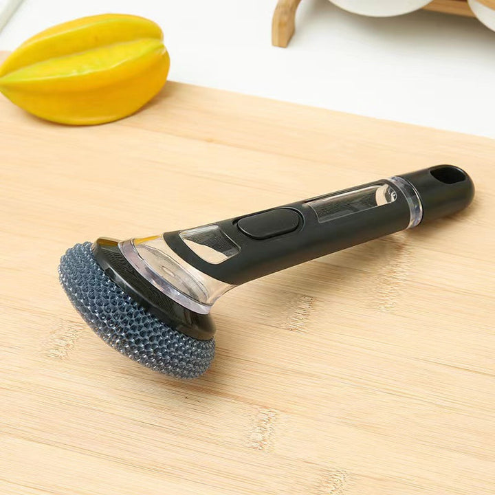 Hand holding a long handle dish cleaning brush with a activated soap dispenser, showing functionality.