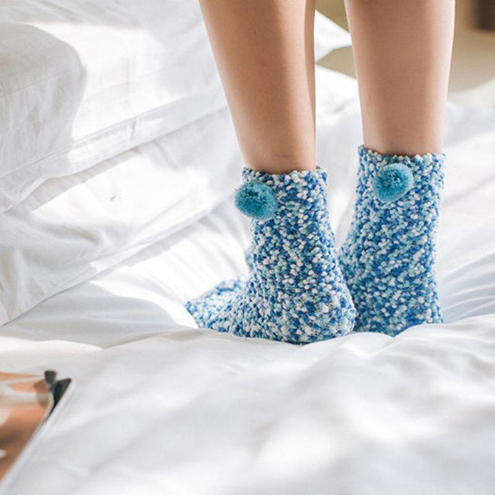 Model wearing pink fluffy cupcake slipper socks, lounging comfortably on a sofa, perfect winter accessory.