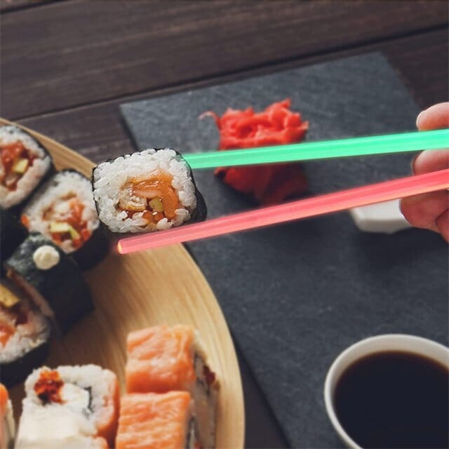 Pair of red Lightsaber LED chopsticks beside a bowl of noodles, ready for use. Reusable dining.