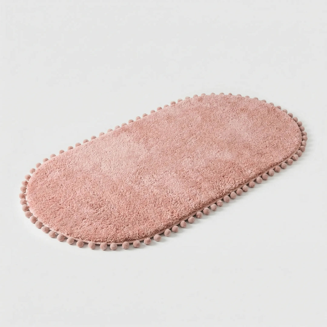 Modern oval bath rug with unique pompom design and wave pattern. Plush, absorbent, non-slip bathroom accent mat.