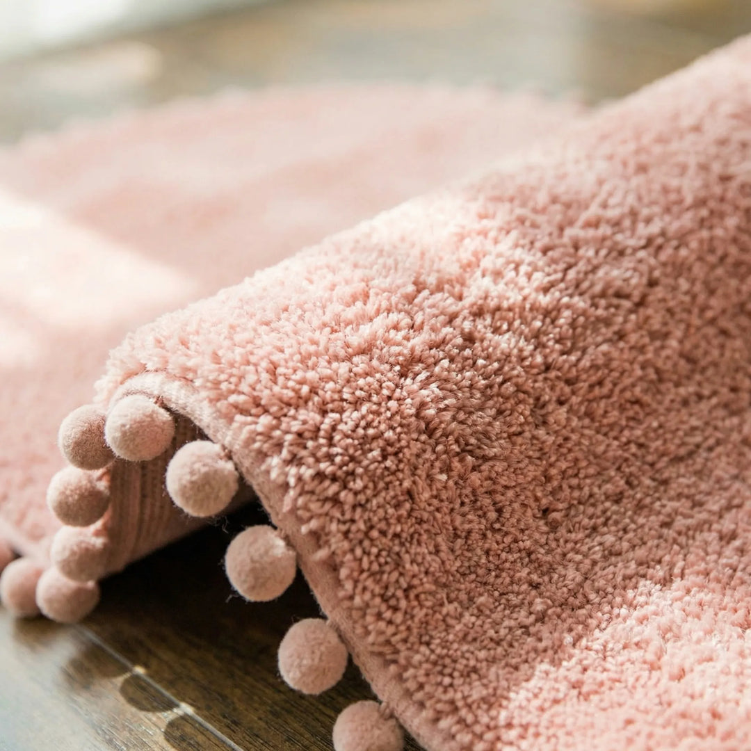 Soft, plush oval pompom bath rug providing absorbent comfort. A modern non-slip bathroom mat for home decor.