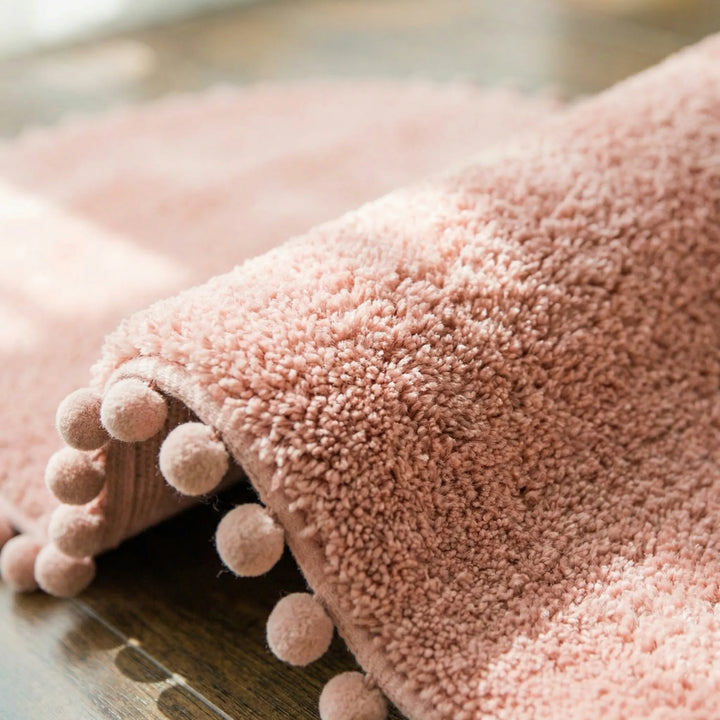 Soft, plush oval pompom bath rug providing absorbent comfort. A modern non-slip bathroom mat for home decor.
