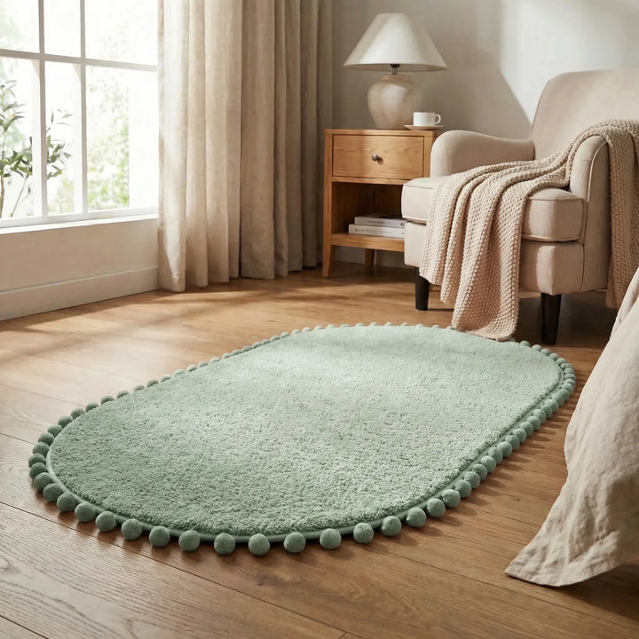 Absorbent & non-slip oval pompom bath rug. Plush statement bathroom mat with a modern wave design for home decor.