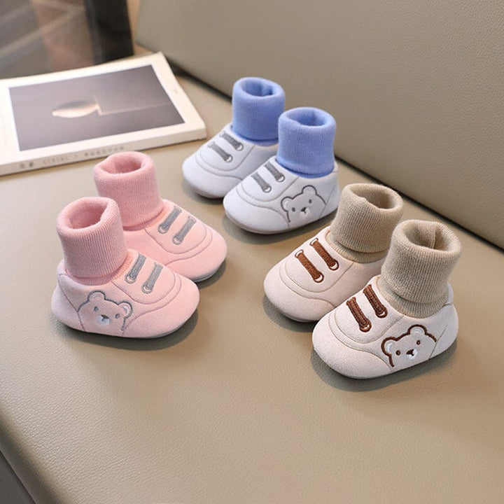Newborn wearing white plush winter booties, ideal soft sole infant footwear