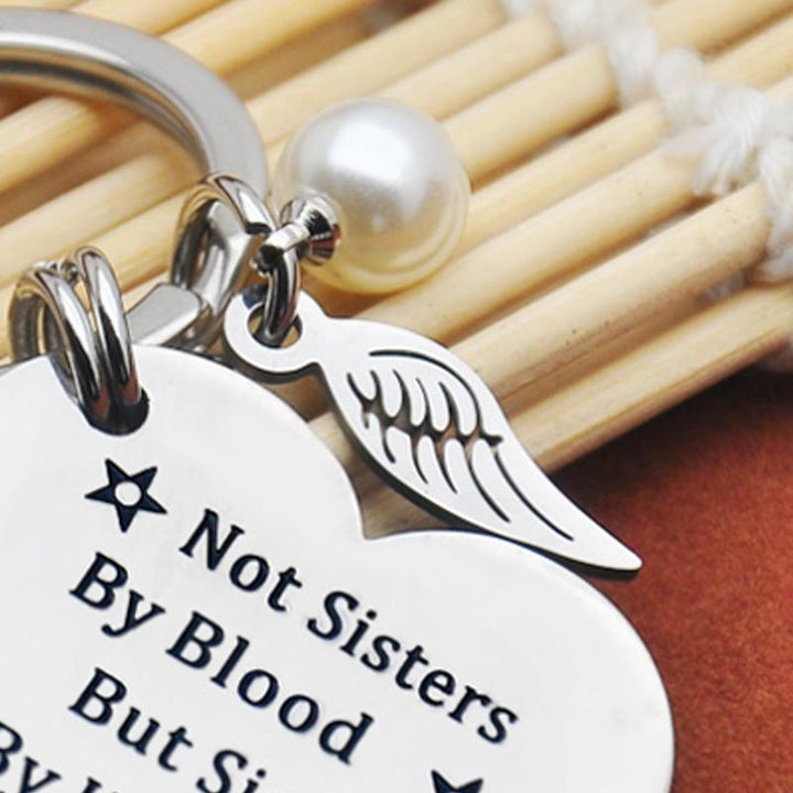 Close-up of a round stainless steel keychain, 'Sisterhood' text clearly visible, friendship accessory.