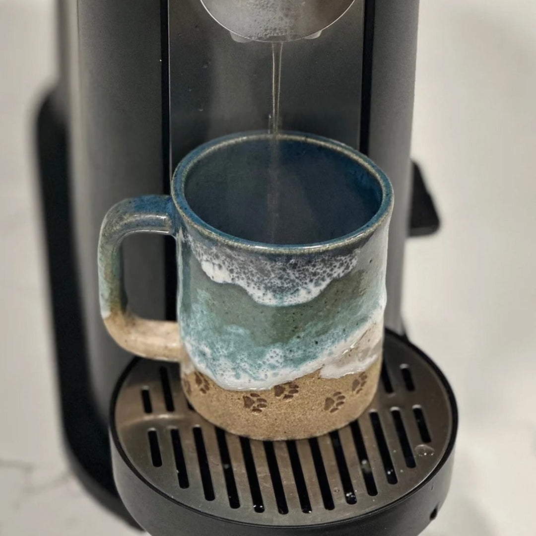 Handmade ceramic coffee mug with an ocean-inspired finish and subtle paw print detail, kitchenware item