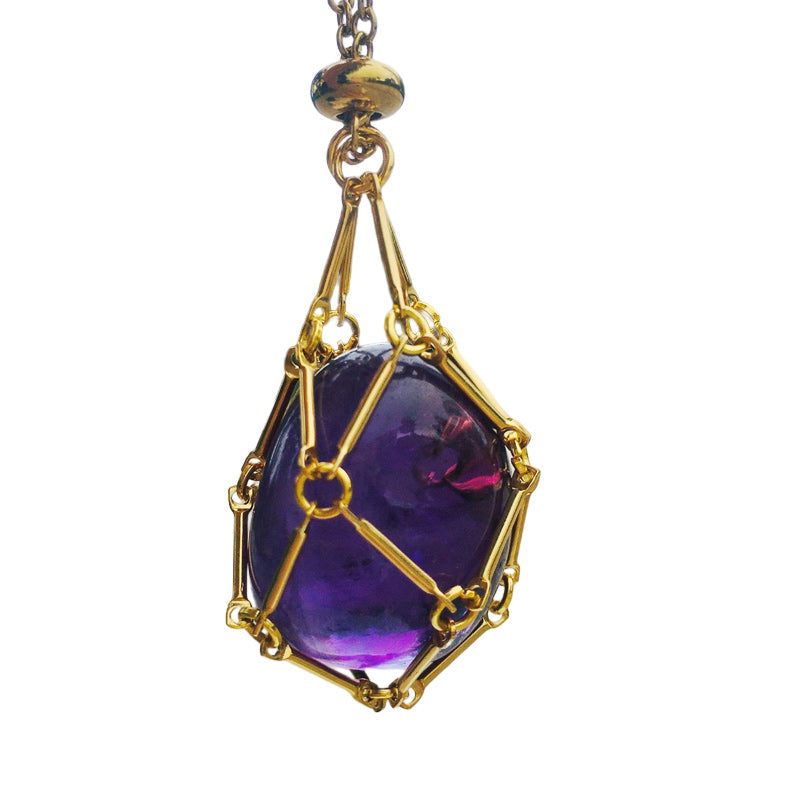 Crystal cage pendant necklace, unisex, beside a collection of healing stones, spiritual