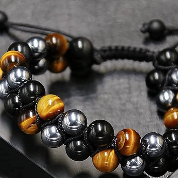 Hand modeling a double-layered unisex bracelet of tiger's eye, obsidian, and hematite beads for spiritual and fashion appeal.