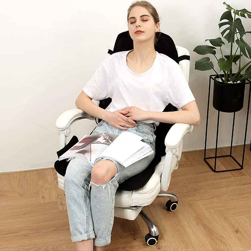Person relaxing in a chair using a portable heated massage cushion for stress & back pain relief.