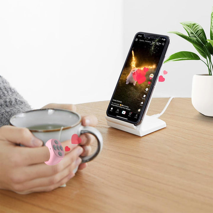 Black Bluetooth phone remote, worn on finger, for hands-free smartphone navigation and camera control.