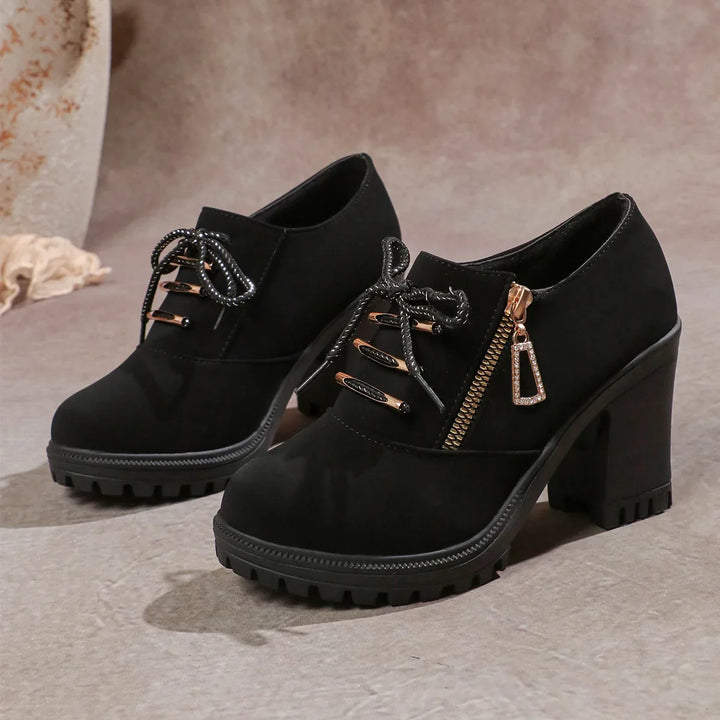 Close-up of the comfortable block heel on a women's black ankle boot with detailed lacing.