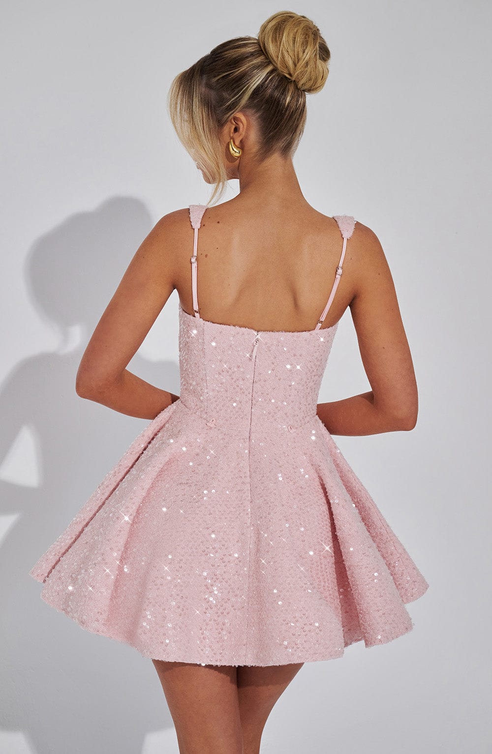 Back view of a women's backless pink sequin mini dress showcasing a large, elegant bow.