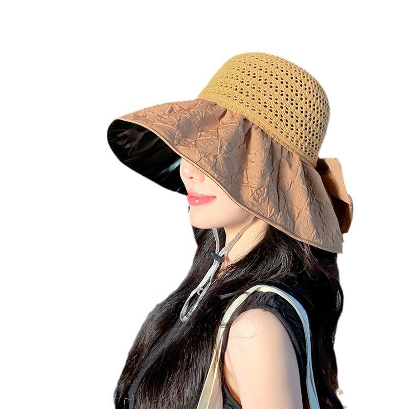 Women's sun hat in papyrus, wide-brim and foldable, with a chic bow, on a sandy beach.