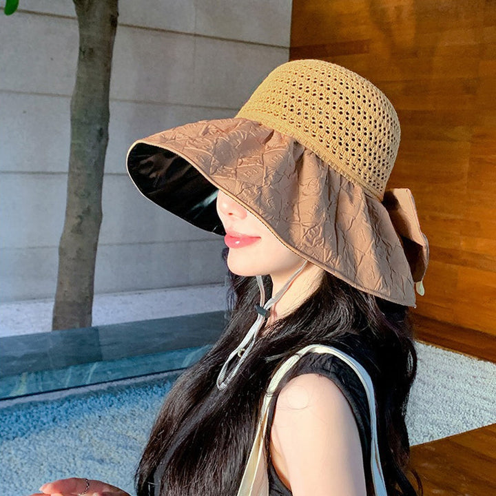 Women's wide-brim sun hat, foldable and made of papyrus, with a bow, worn by a model outdoors.