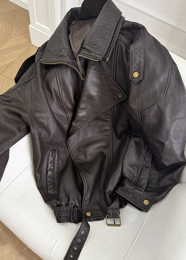 Close-up of a women's oversized faux leather bomber jacket in brown with a cinched belt.