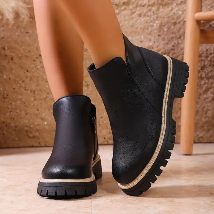 Pair of women's premium leather ankle boots, black, showing the textured lug sole and side zipper.