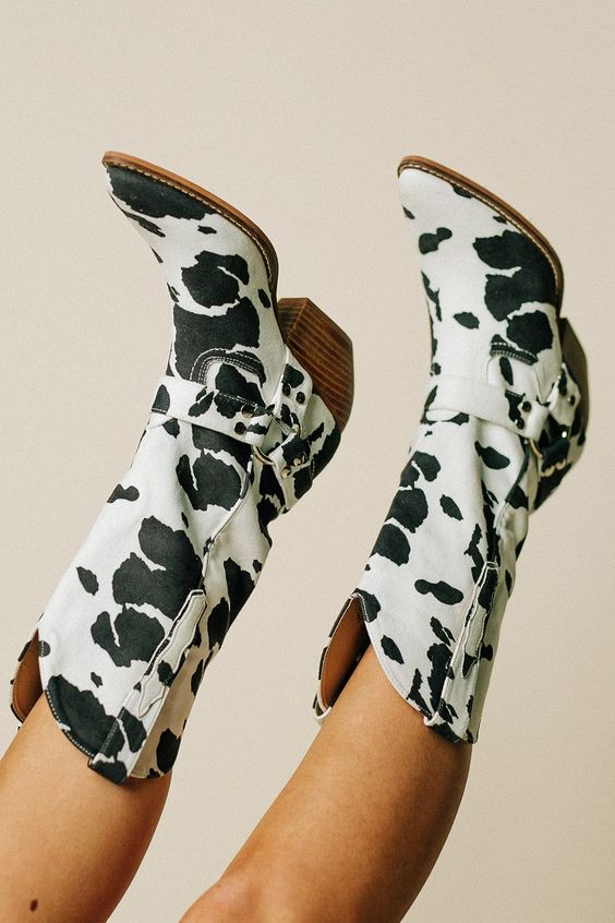 Trendy women's boots with a striking cow print pattern and a fashionable belt, ideal for a bold cowgirl statement.