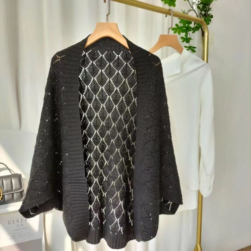 White knit short cardigan draped on a hanger, showcasing its diamond hollow pattern.