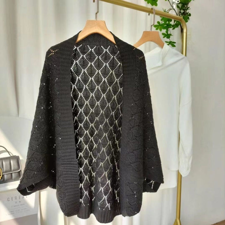 White knit short cardigan draped on a hanger, showcasing its diamond hollow pattern.