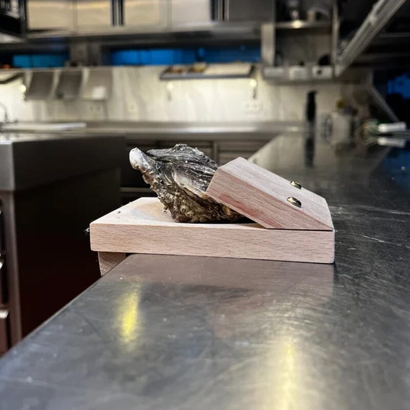 Chef using a wooden oyster shucking clamp to prepare seafood, kitchen gadget